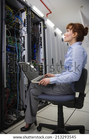 Technician sitting on swivel chair using laptop to diagnose servers in large data center