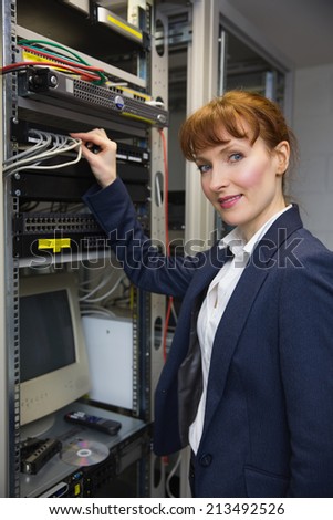 Pretty computer technician smiling at camera while fixing server in large data center