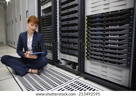 Technician sitting on floor beside server tower using tablet pc in large data center