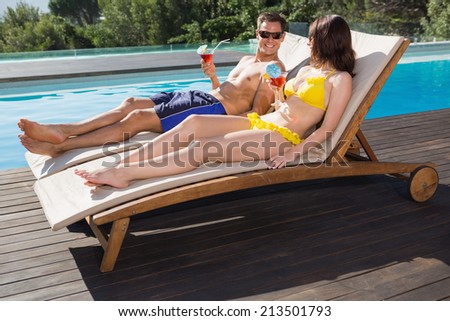 Romantic young couple with drinks sitting by swimming pool