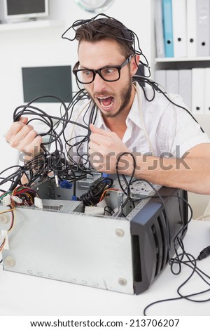 Angry computer engineer pulling wires in his office