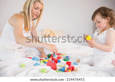 Side view of mother and daughter playing with building blocks on bed at home