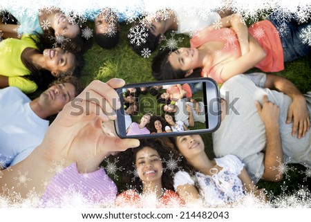 Hand holding smartphone showing multiethnic friends lying down in park