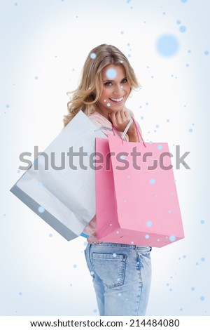 A woman looking back at the camera is carrying shopping bags over her shoulder against snow falling