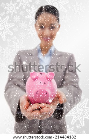 Portrait of a happy businesswoman showing a piggy bank against snowflakes on silver