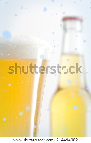 Snow falling against bottle and glass of beer against a white background