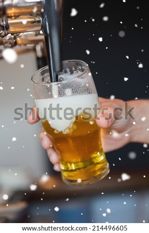 Hand holding glass filling beer against snow falling