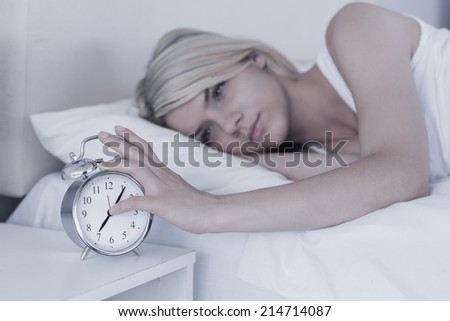 Young woman extending hand to alarm clock in bed at home