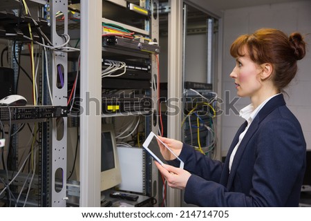 Pretty technician using tablet pc while looking at server in large data center