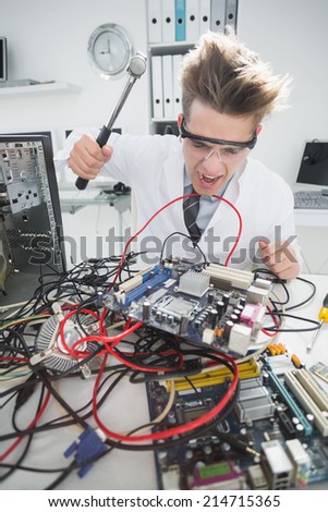Angry computer engineer holding hammer over console in his office