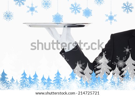Hand with gloves holding a silver tray against snowflakes and fir trees