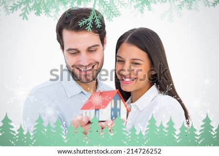 Attractive young couple holding a model house against frost and fir trees in green