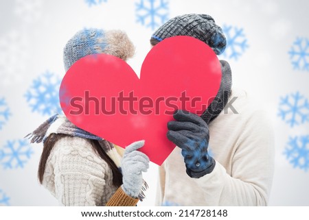 Attractive young couple in warm clothes holding red heart against snowflakes