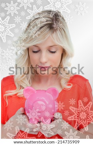 Young woman looking at a piggy bank held by her hands against snowflakes on silver