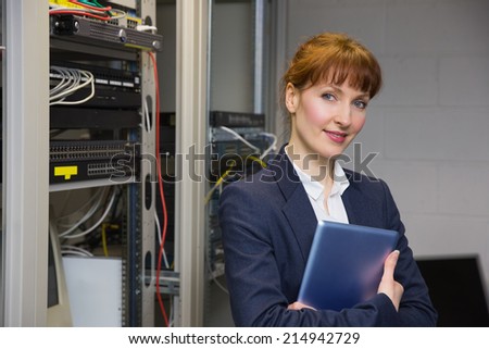 Pretty technician smiling at camera beside open server in large data center