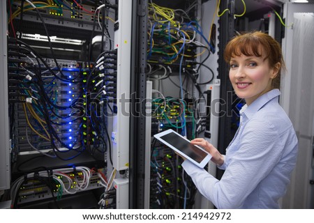 Smiling technician using tablet pc while analysing server in large data center