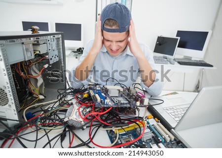 Confused computer engineer working on broken console with laptop in his office
