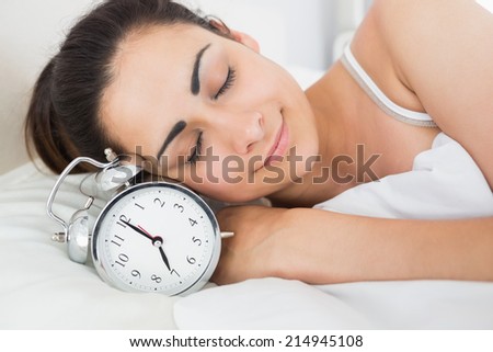 Beautiful young woman sleeping in bed with alarm clock at home