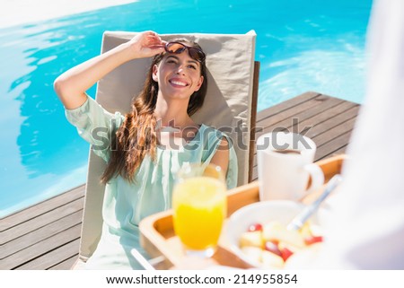 Smiling young woman looking at cropped waiter with breakfast tray by the pool