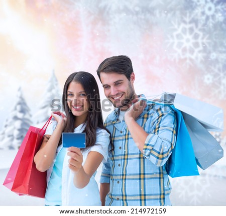 Couple with shopping bags and credit card against snowy landscape with fir trees