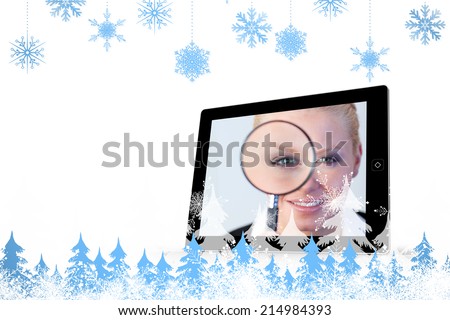 Snowflakes and fir trees against businesswoman holding magnfying glass on tablet screen