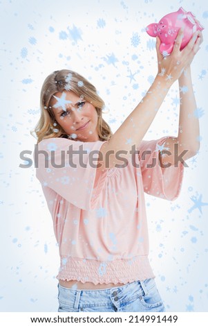 Disappointed woman holds a piggy bank up over her head against snow falling
