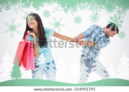 Attractive young man pulling his shopaholic girlfriend against snowflakes and fir tree in green