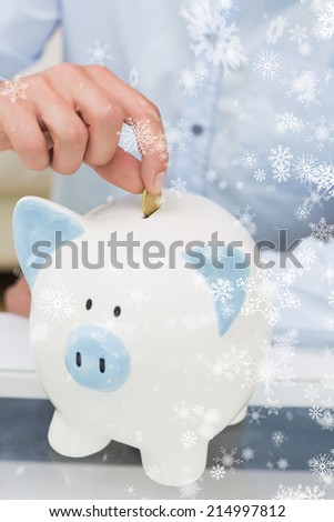 Closeup mid section of a man putting coin into piggy bank against snow falling