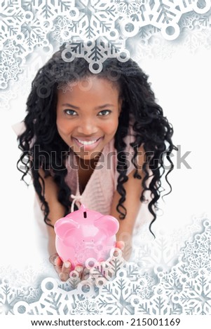 A young woman smiling at the camera is holding a piggy bank in her hands against snowflakes on silver