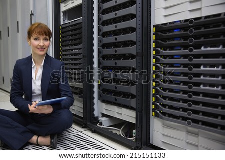 Technician sitting on floor beside server tower using tablet pc in large data center