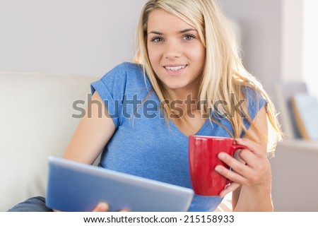 Relaxed beautiful young woman using digital tablet while drinking coffee in the living room at home