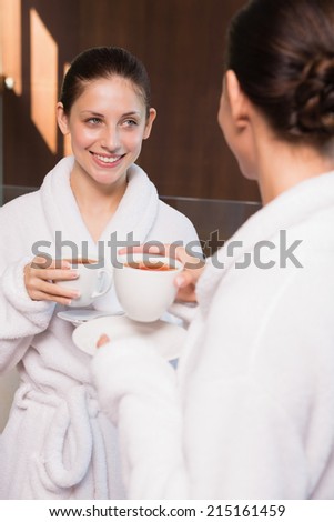 Two smiling young women in bathrobes having tea