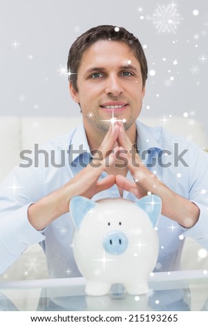 Handsome casual man with piggy bank in living room against snow falling