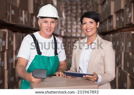 Warehouse worker scanning box with manager holding tablet pc in a large warehouse