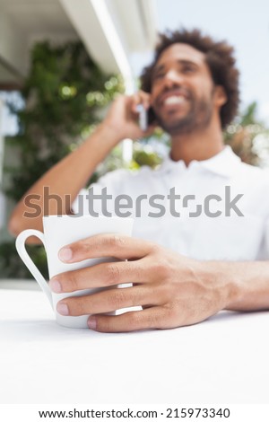 Smiling man on the phone having coffee outside at the coffee shop