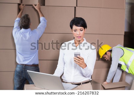 Warehouse manager using laptop and texting on phone in a large warehouse