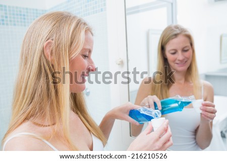 Happy woman pouring blue mouthwash at home in the bathroom