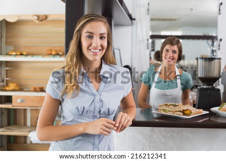 Pretty waitress and customer smiling at camera at the coffee shop