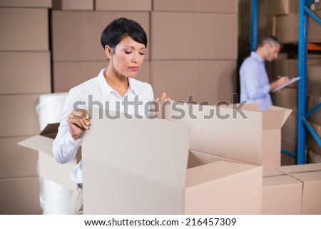 Pretty warehouse manager looking in box in a large warehouse
