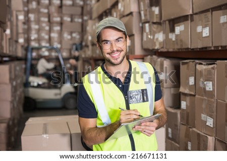 Warehouse worker smiling at camera with clipboard in a large warehouse