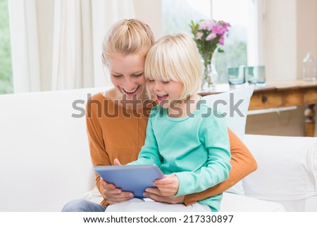 Happy mother and daughter on the couch using tablet at home in the living room