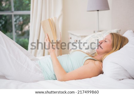 Happy blonde reading her book at home in the bedroom