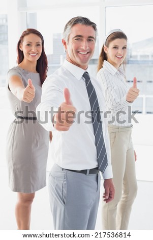 Smiling businessman giving thumbs up with co-workers