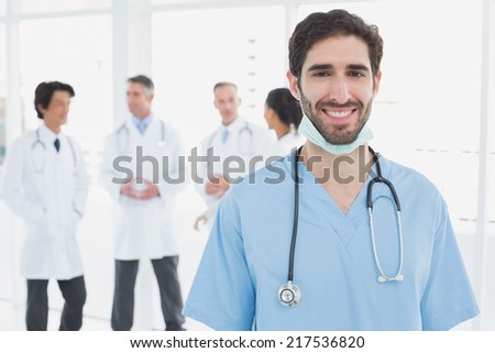Smiling doctor looking at camera with co-workers behind him