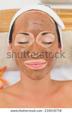 Smiling brunette getting a mud treatment facial in the health spa