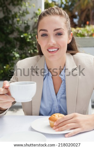 Beautiful businesswoman having a coffee and muffin outside at the coffee shop