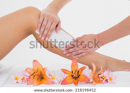 Mid section of therapist waxing womans leg at spa center