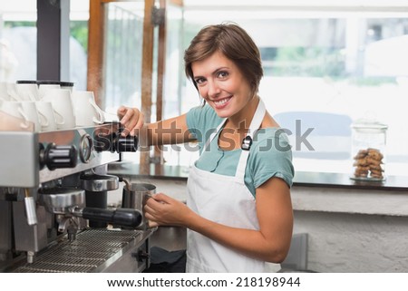 Pretty barista steaming jug of milk at coffee machine at the coffee shop