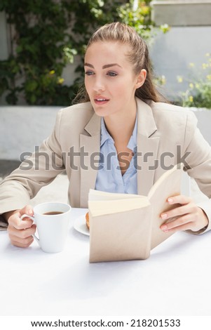 Beautiful businesswoman having a coffee reading book outside at the coffee shop