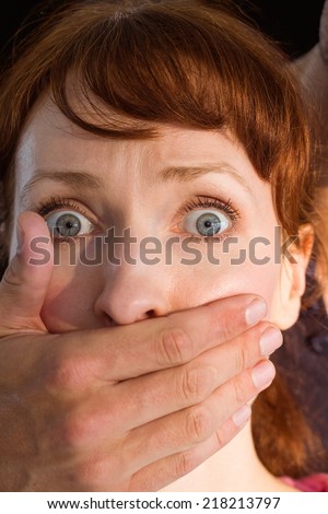 Terrified woman with covered mouth on black background